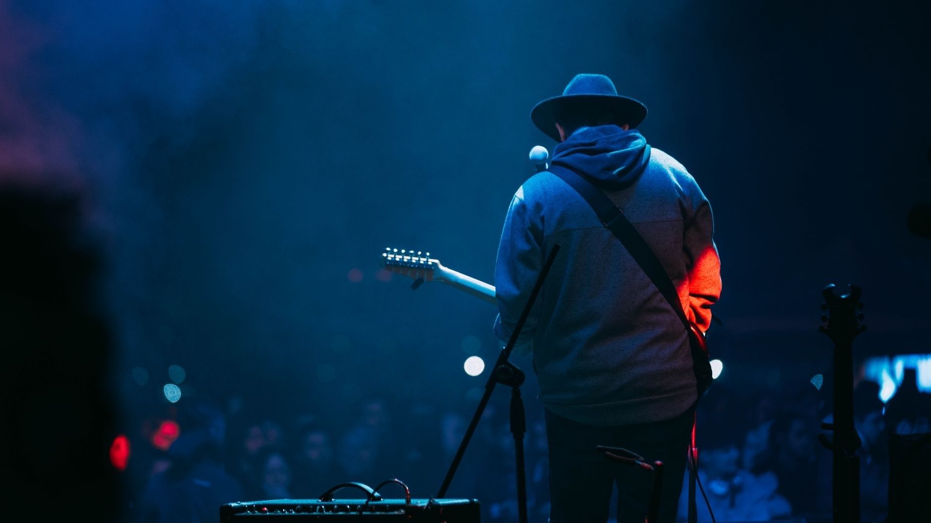 Gitarist med hatt spiller på en blåbelyst scene foran publikum